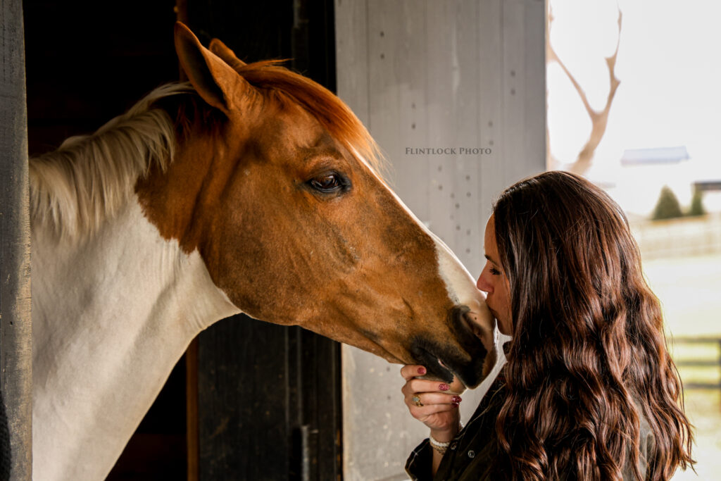 A girl kissing a horse in a barn stall.